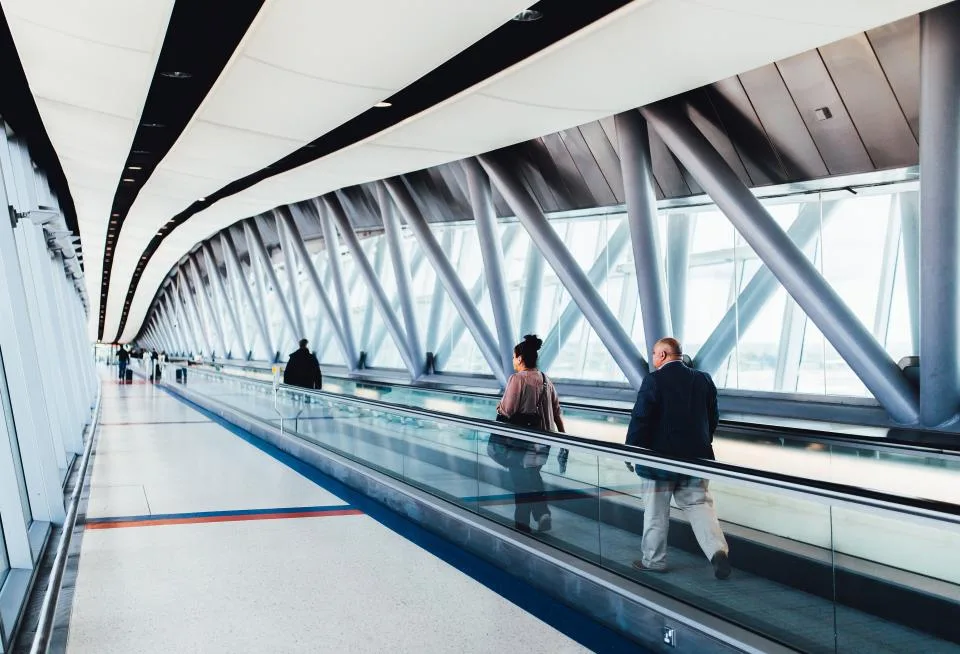 Corredor envidraçado de aeroporto com esteira rolante e passageiros de costas ao fundo, ilustrando a autorização de viagem ao exterior de filhos de pais separados