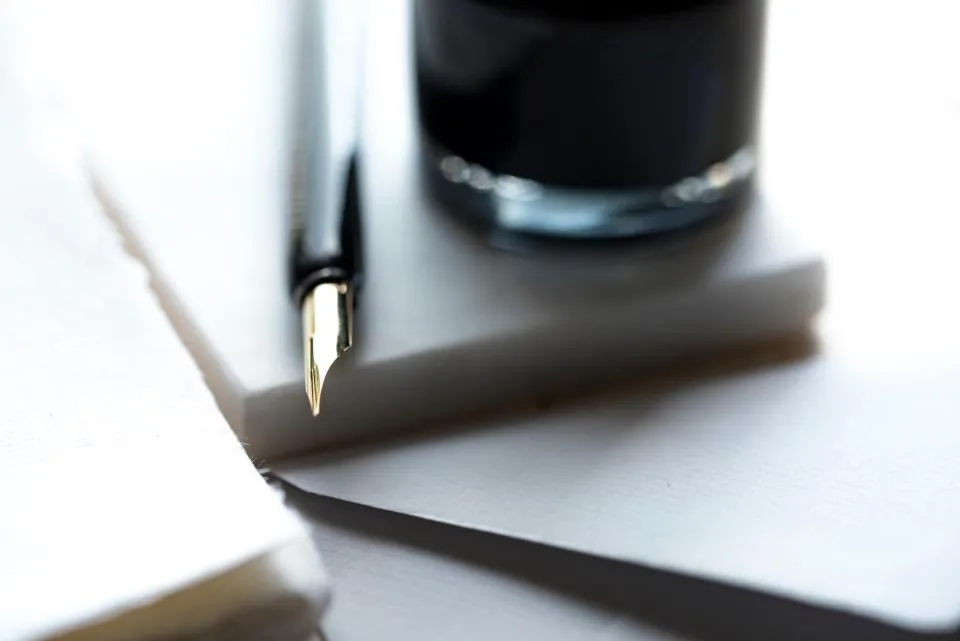 Caneta-tinteiro apoiada sobre folhas de papel em branco ao lado de um tinteiro escuro, ilustrando o inventário extrajudicial DF feito por escritura